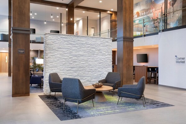 A lobby with a stone partition, two grey armchairs, a coffee table, and a sign for the Comer Market. - Fairfield Inn & Suites by Marriott Franklin Cool Springs (Franklin)