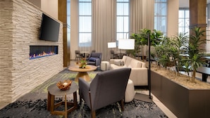 Un hall d’hôtel moderne avec un mur en pierre, un téléviseur à écran plat, une cheminée, des fauteuils confortables et de grandes fenêtres.