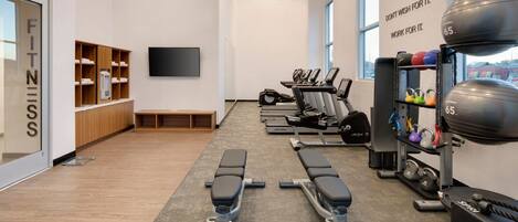 Un gimnasio moderno con equipo de ejercicio, un televisor y decoración inspiradora en las paredes.