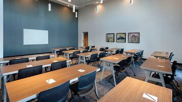 A conference room with multiple tables and chairs, a projector screen, and framed pictures on the wall.