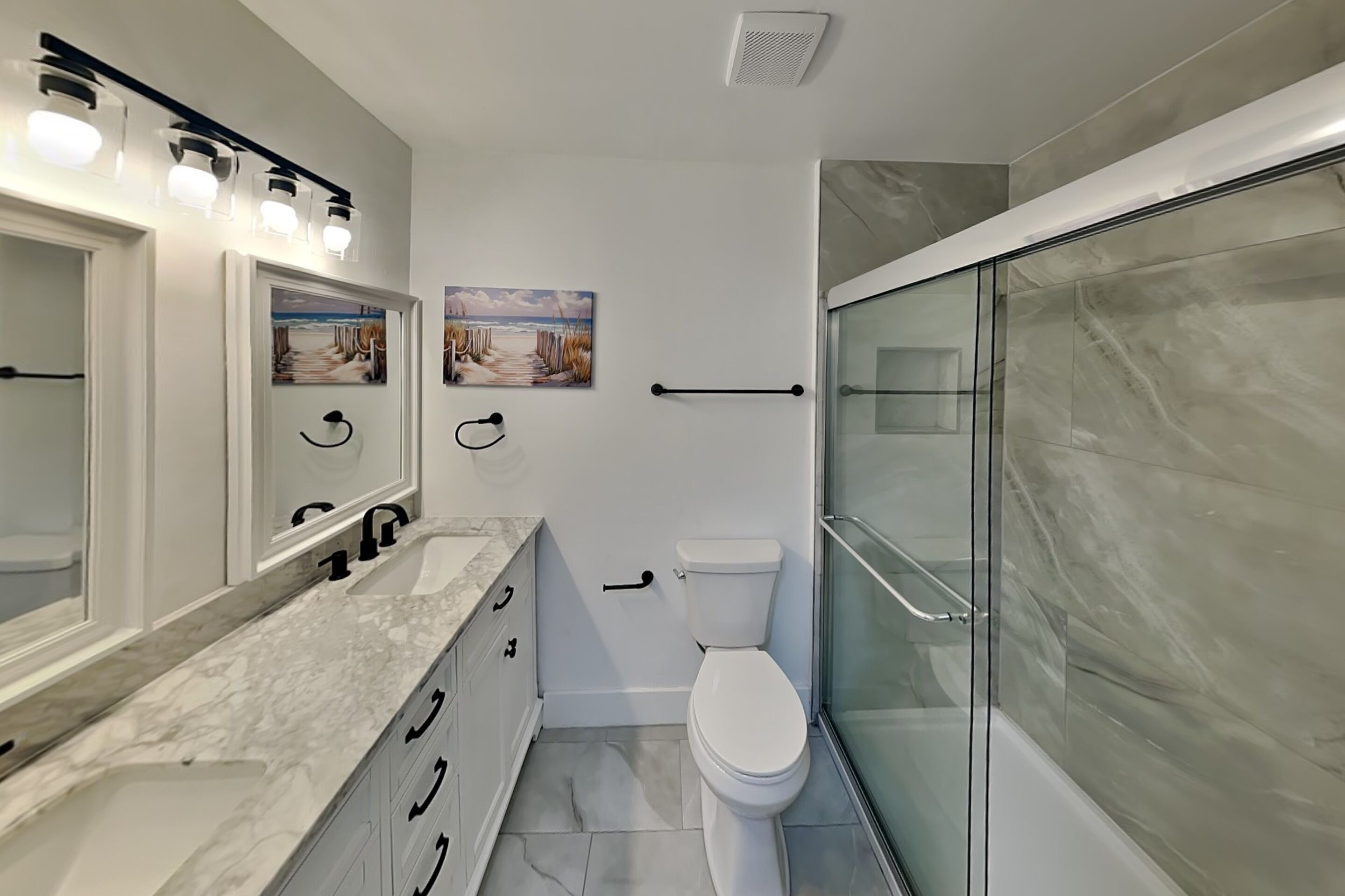 Une salle de bain avec un meuble-lavabo en marbre, des toilettes, une douche en verre et deux tableaux accrochés au mur.