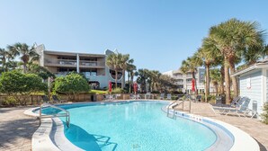 A swimming pool with a 5 ft 9 in depth, surrounded by lounge chairs and palm trees. - Hibiscus 301-A by Distinctive Beach Rentals (St. Augustine)