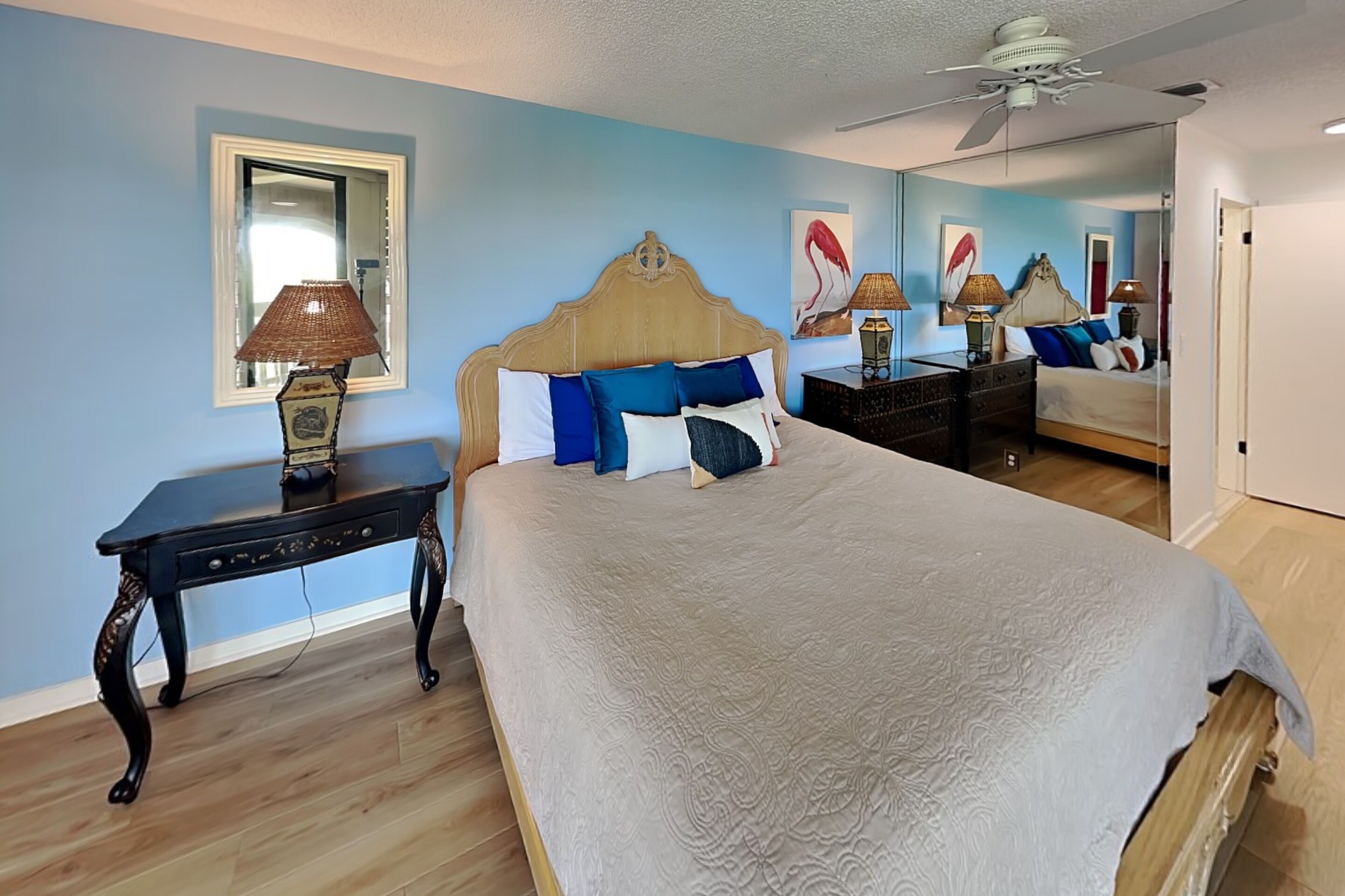 A bedroom with a large bed, a nightstand, a dresser, a mirror, and a ceiling fan.