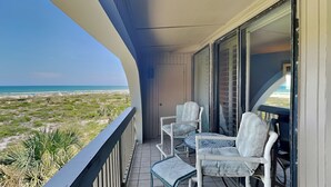 A balcony with a view of the beach, two chairs, a table, and a door. - Hibiscus 301-A by Distinctive Beach Rentals (St. Augustine)