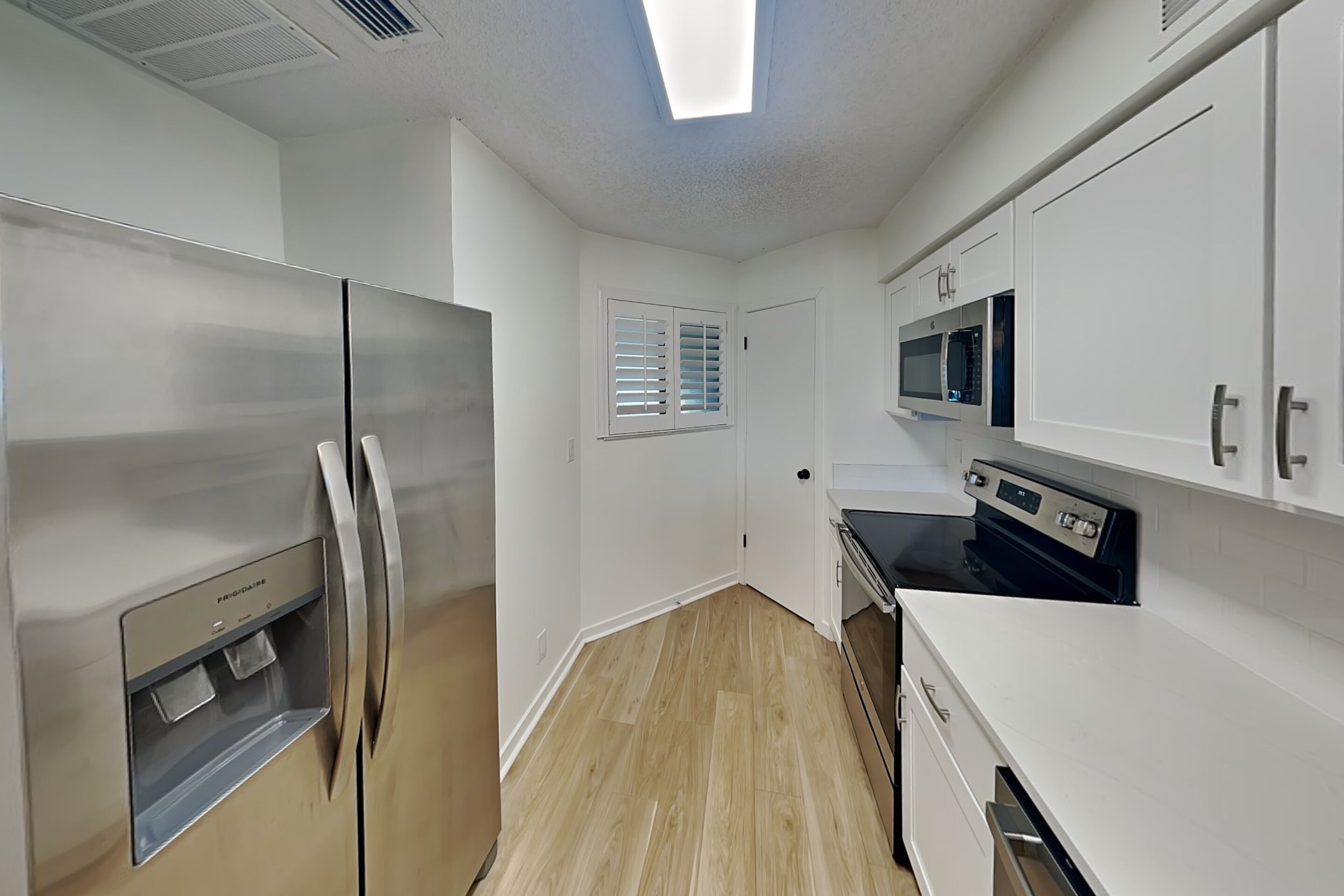 Une cuisine moderne dotée d’appareils électroménagers en acier inoxydable, de meubles blancs et d’un plancher en bois.