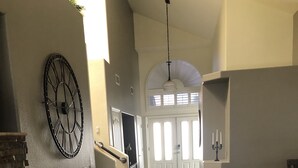 Ein geräumiger Korridor mit dunklem Holzboden, einer großen Wanduhr und einer Treppe zu einem hellen Raum mit großen Fenstern.