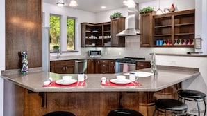 A modern kitchen with dark wood cabinets, a central island with bar stools, a microwave, stove, and a sink. - Beautiful Lake Area Home, Gas Grill - Close to Downtown Florence & Dunes (Florence)
