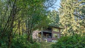 A two-story cabin nestled in a forest, with a visible deck and large windows. - Beautiful Lake Area Home, Gas Grill - Close to Downtown Florence & Dunes (Florence)