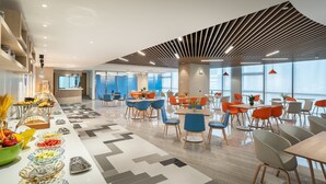 A modern dining area with multiple tables and chairs, a buffet with various food items, and large windows providing natural light. - Holiday Inn Express Yangjiang City Center by IHG (Yangjiang)