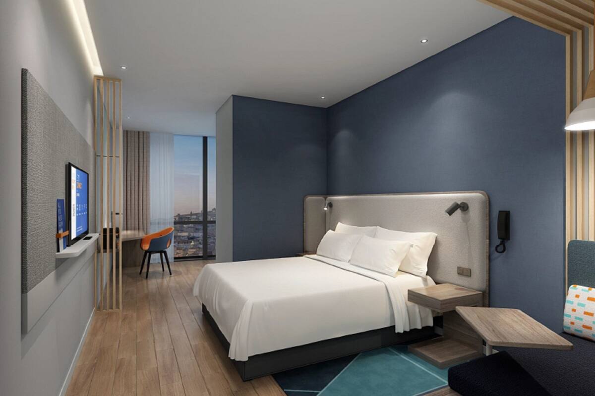 A modern hotel room with a large bed, a desk, a chair, and a view of the city.