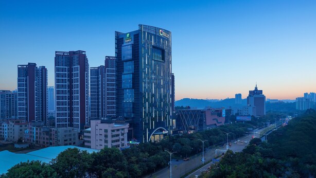 A modern high-rise building with a glass facade, surrounded by other high-rise buildings and a busy street with cars. - Holiday Inn Express Yangjiang City Center by IHG (Yangjiang)