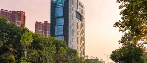 A modern hotel with a prominent 'Hotel Express' sign, surrounded by lush greenery and other buildings.