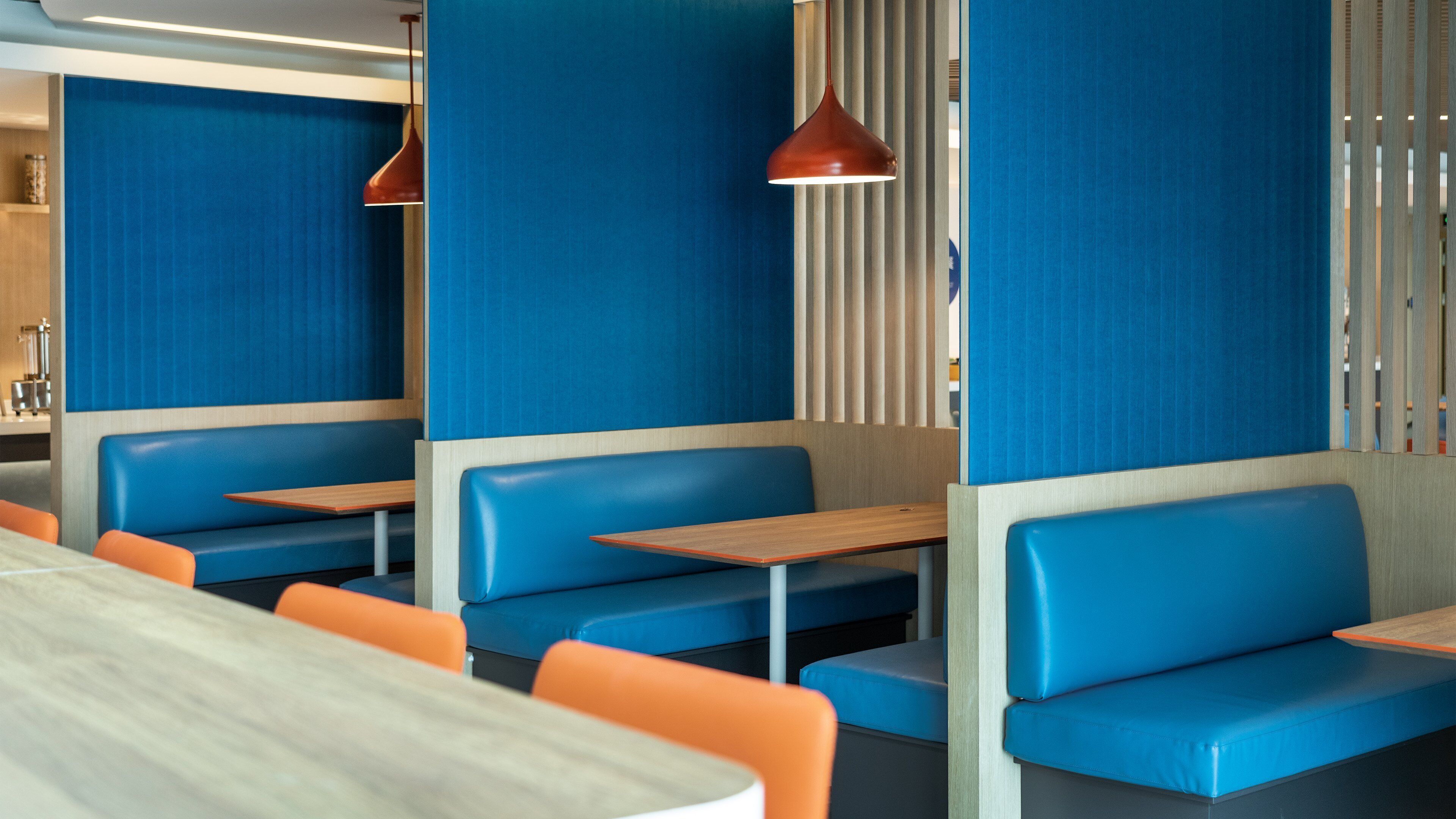 Un interno di ristorante con banquette e tavoli, sedute blu e arancioni e illuminazione a sospensione.