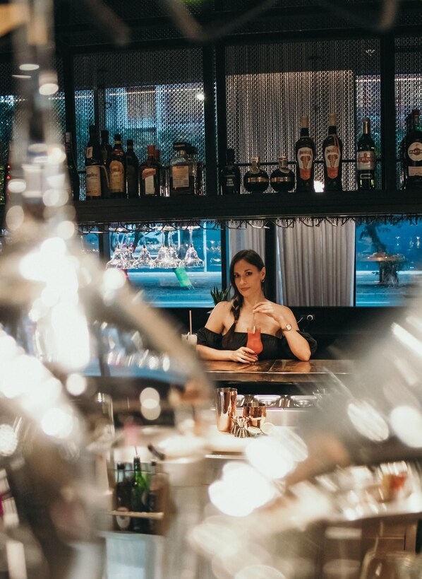 A bar area with a bartender, shelves of liquor bottles, and a view of the cityscape through the window. - The Rockefeller Hotel by Newmark (Cape Town)