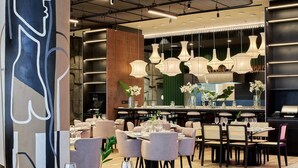 A modern restaurant interior with round tables, cushioned chairs, and pendant lighting. - The Rockefeller Hotel by Newmark (Cape Town)