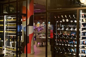A wine cellar with racks of bottles, a neon sign, and a bar area with glasses and bottles.