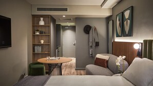 A compact hotel room with a bed, a small round table, a bookshelf, and a TV. - The Rockefeller Hotel by Newmark (Cape Town)