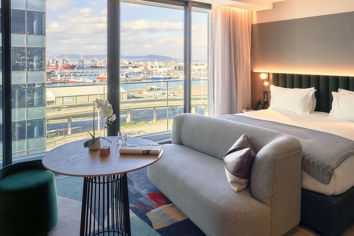 A hotel room with a bed, a sofa, a small table, and a view of a harbor.