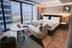 A hotel room with a large bed, a sofa, a small table, and a view of the cityscape. - The Rockefeller Hotel by Newmark (Cape Town)