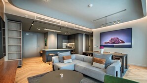 A modern living room with a grey sofa, a round coffee table, and a TV mounted on the wall. - The Rockefeller Hotel by Newmark (Cape Town)