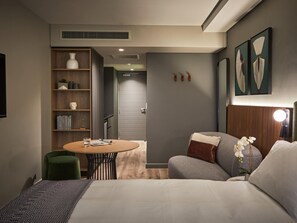 Une chambre d’hôtel moderne, équipée d’un lit, d’une table ronde, d’une chaise verte, d’une bibliothèque et d’une lampe fixée au mur.