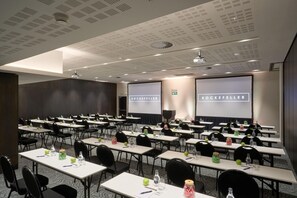 A conference room with multiple tables, chairs, and presentation screens displaying the name "ROCKEFELLER". - The Rockefeller Hotel by Newmark (Cape Town)