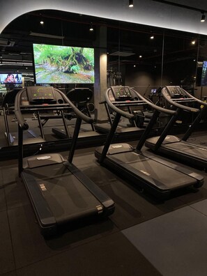 A gym with treadmills, exercise equipment, and a large screen displaying a nature scene.
