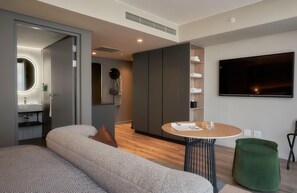 A modern living room with a sofa, a round table, a flat-screen TV, and a wardrobe. - The Rockefeller Hotel by Newmark (Cape Town)