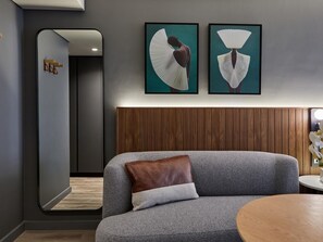 A modern room with a grey sofa, a wooden headboard, and two framed artworks above the sofa. - The Rockefeller Hotel by Newmark (Cape Town)