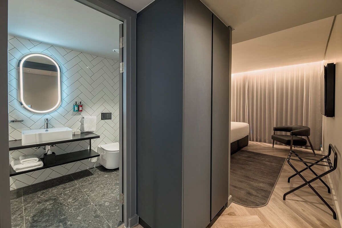 A modern bathroom with a herringbone tile backsplash, a round mirror with underglow lighting, a white sink, and a toilet.