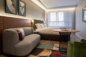 A hotel room with a bed, a sofa, a small table, and a green chair.