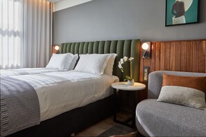 A hotel room with a bed, a chair, a small table with a vase of flowers, and a painting on the wall. - The Rockefeller Hotel by Newmark (Cape Town)