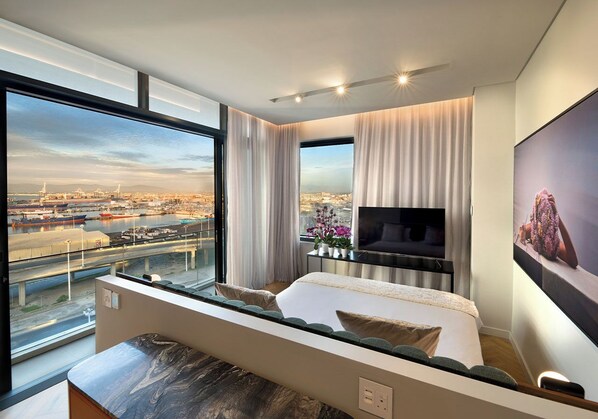 A modern hotel room with a large window offering a city view, a flat-screen TV, and a comfortable bed. - The Rockefeller Hotel by Newmark (Cape Town)