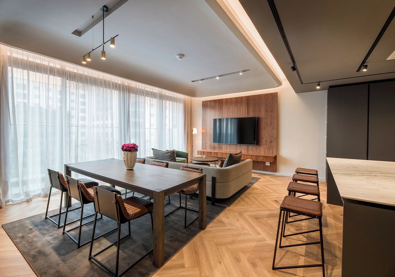 A modern living room with a wooden dining table, sofa, and TV mounted on the wall.