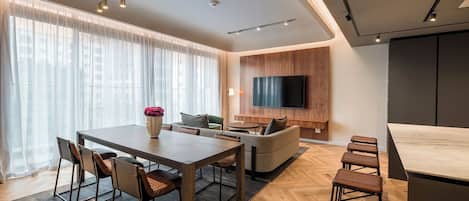 A modern living room with a wooden dining table, sofa, and TV mounted on the wall.