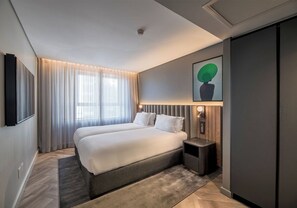 A modern hotel room with a large bed, a bedside table, a wall-mounted TV, and a painting. - The Rockefeller Hotel by Newmark (Cape Town)