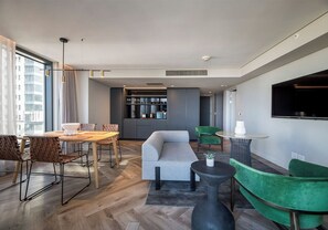 A modern living room with a dining area, a grey sofa, green chairs, and a TV mounted on the wall. - The Rockefeller Hotel by Newmark (Cape Town)