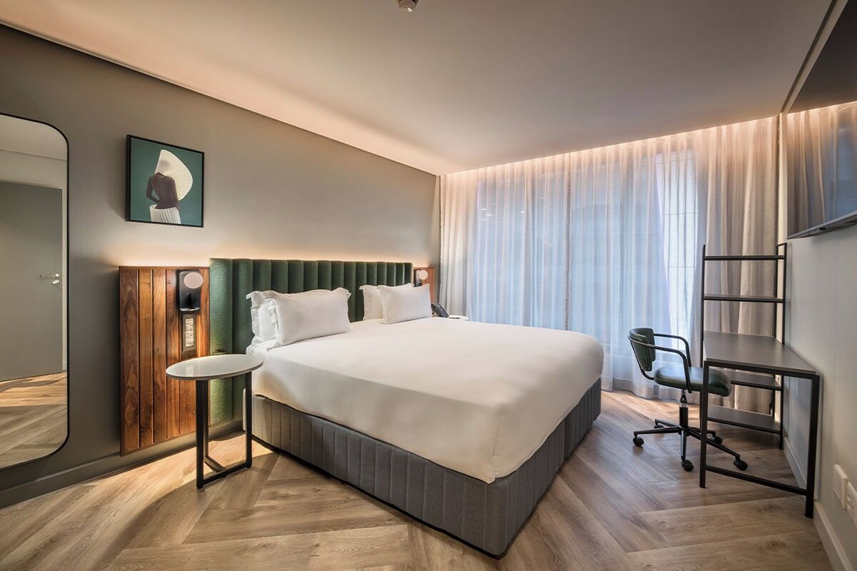 A modern hotel room with a large bed, a desk, and a chair.