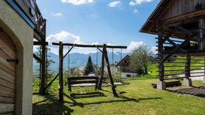A wooden cabin with a swing set and a bench in a grassy area, overlooking a valley with mountains in the background. - Pure nature with amazing view (Podjelje)
