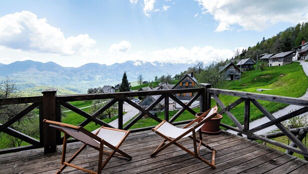 A wooden deck with two lounge chairs and a potted plant, overlooking a village with houses and mountains in the background. - Pure nature with amazing view (Podjelje)