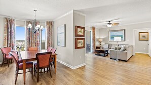A spacious living room with a large dining table and chairs, a sofa, and a ceiling fan.