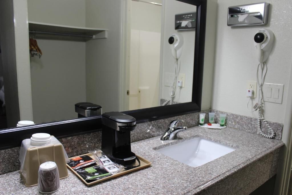 Une salle de bain d’hôtel avec un comptoir en granit, un lavabo, un miroir, un sèche-cheveux et une machine à café.