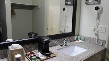 Une salle de bain d’hôtel avec un comptoir en granit, un lavabo, un miroir, un sèche-cheveux et une machine à café.