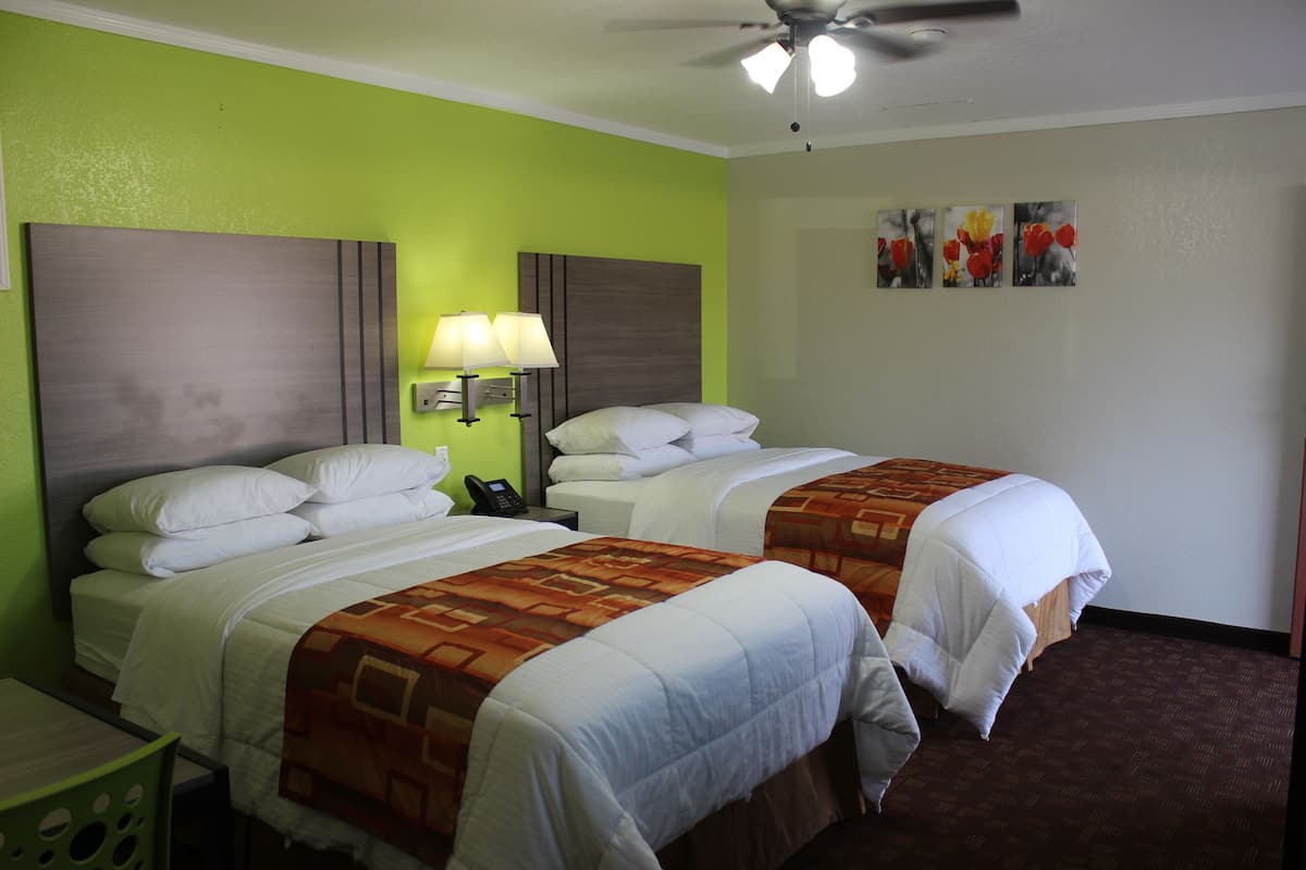 Habitación de hotel con dos camas, un escritorio, una silla, un ventilador de techo y obras de arte en la pared.