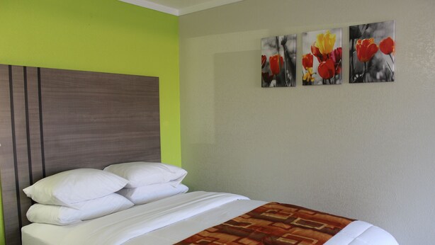 Una habitación de hotel con una cama, un cabecero y tres cuadros de flores colgados en la pared.