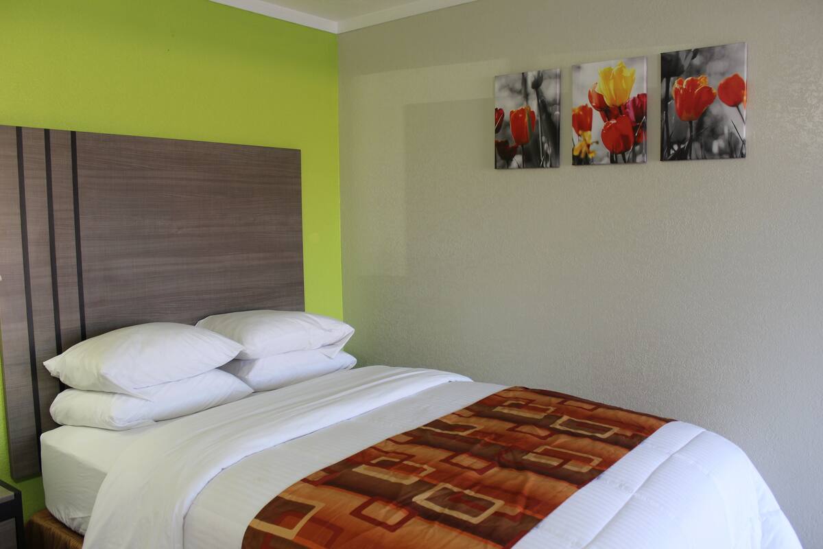 Una habitación de hotel con una cama, un cabecero y tres cuadros de flores colgados en la pared.