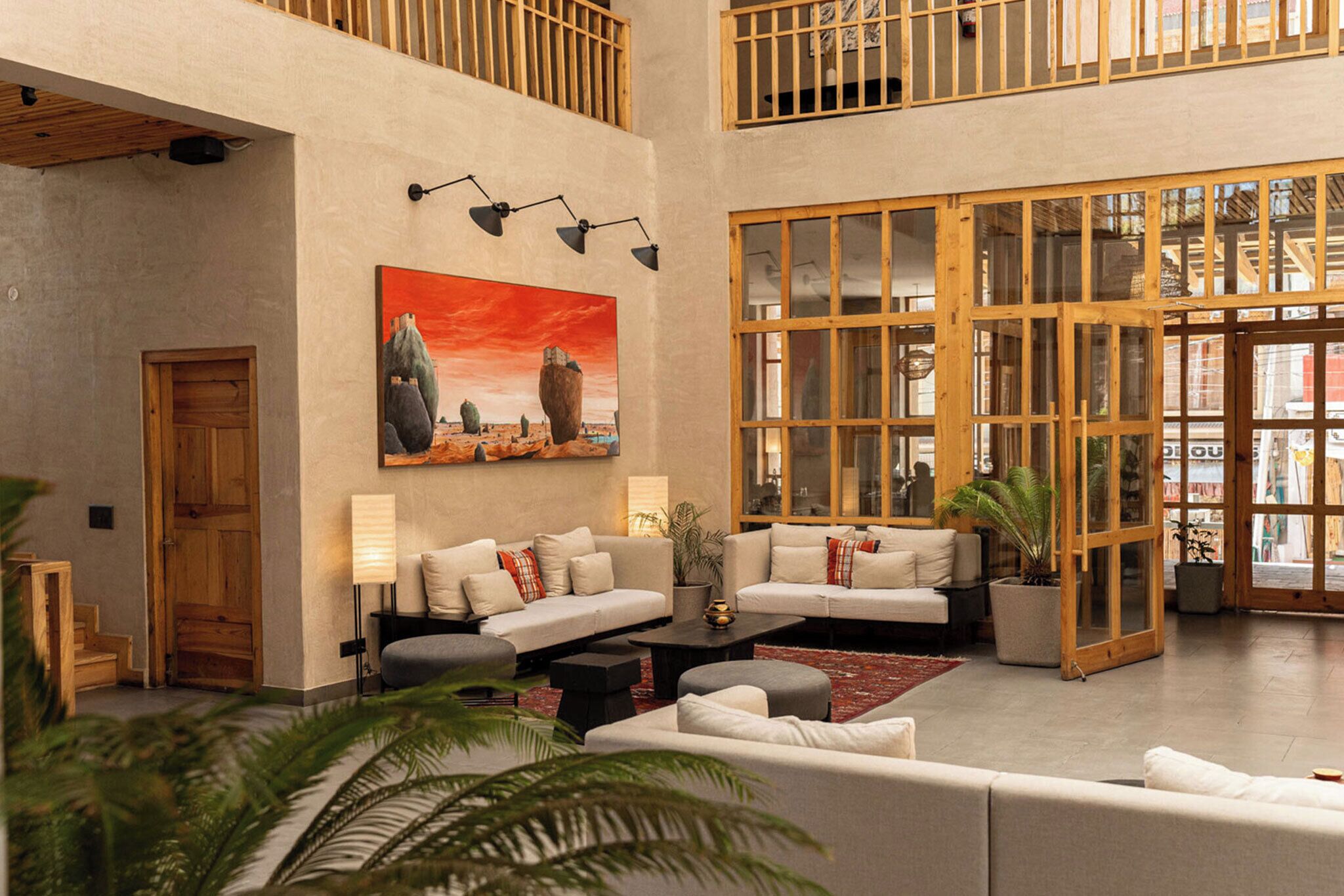 A spacious lobby with high ceilings, a large painting of a desert landscape, and a modern seating area with sofas and a coffee table.