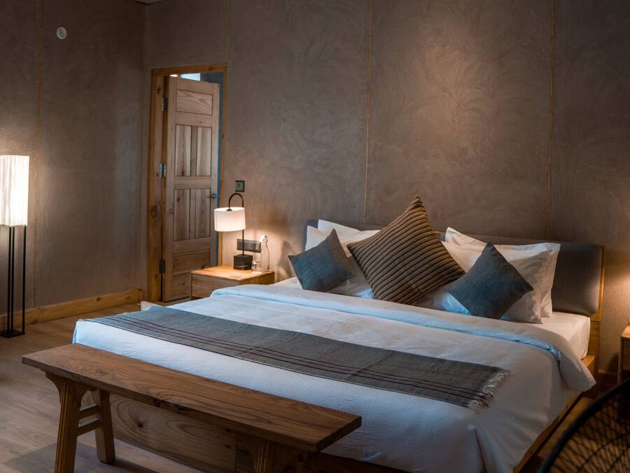 A bedroom with a large bed, bedside tables, a bench, and a fan.