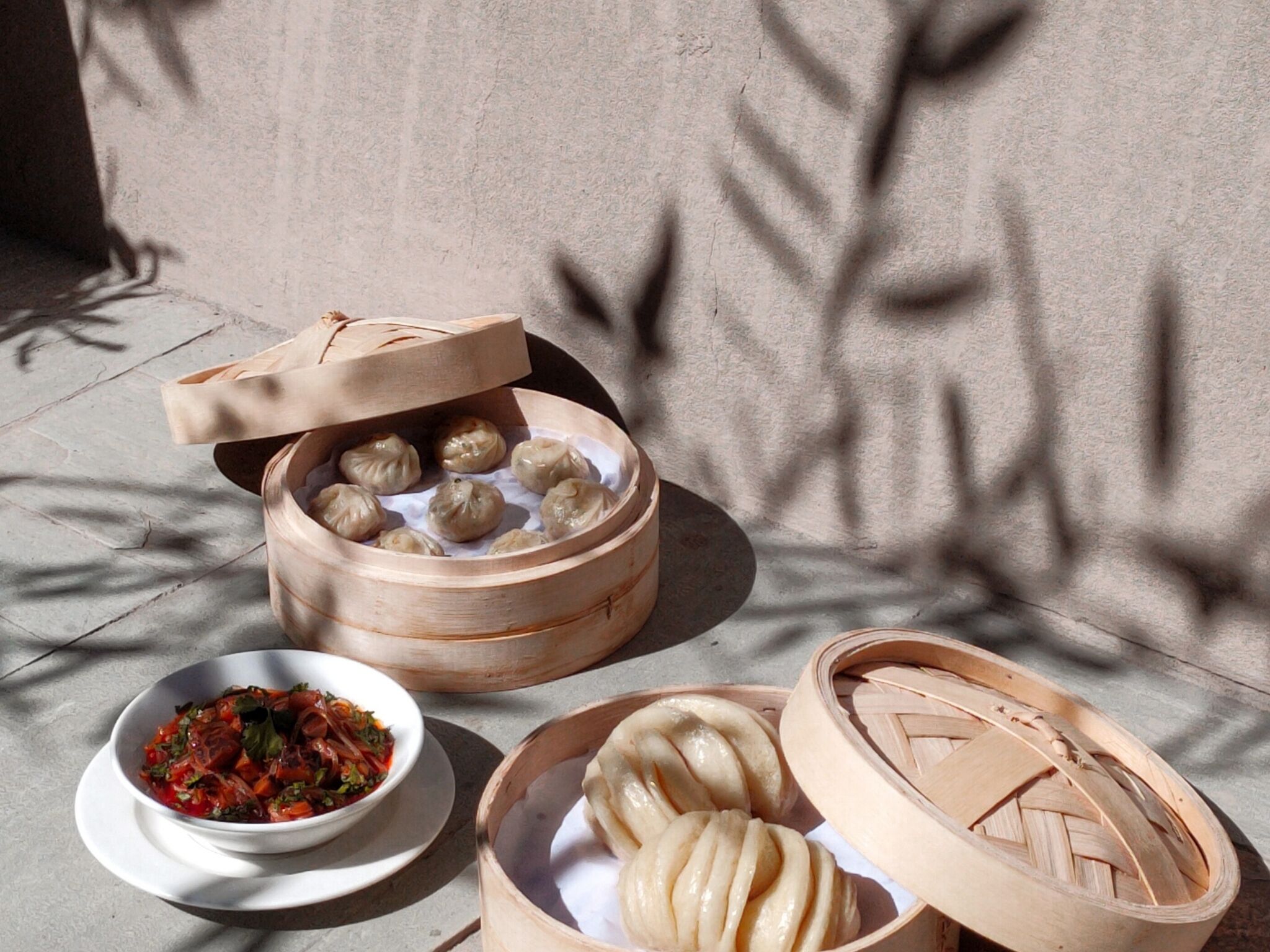 A bamboo steamer with dumplings, a bowl of sauce, and a plate of dumplings.