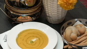 A bowl of soup with a decorative lid, a white vase with flowers, and a basket of breadsticks.